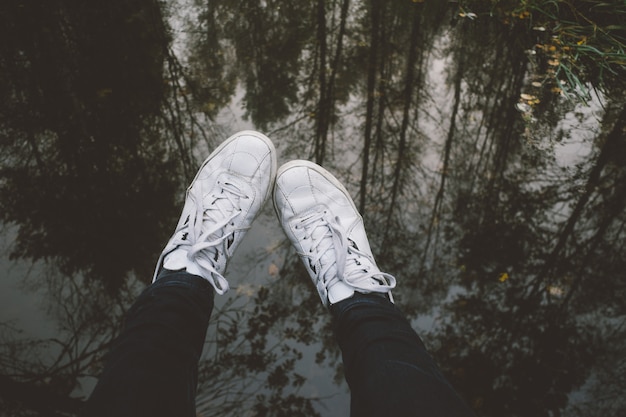 Photo jambes mâles en baskets contre l'eau avec reflet des arbres