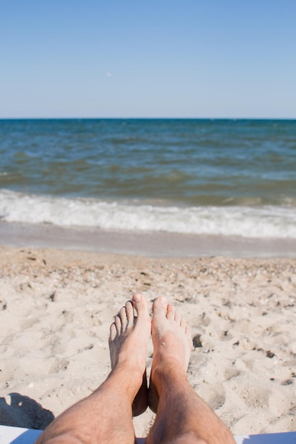 Jambes masculines sur une chaise longue contre la mer