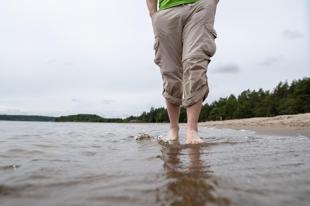 Les jambes masculines pieds nus en pantalon retroussé se tiennent calmement sur le fond sablonneux dans l'eau du lac