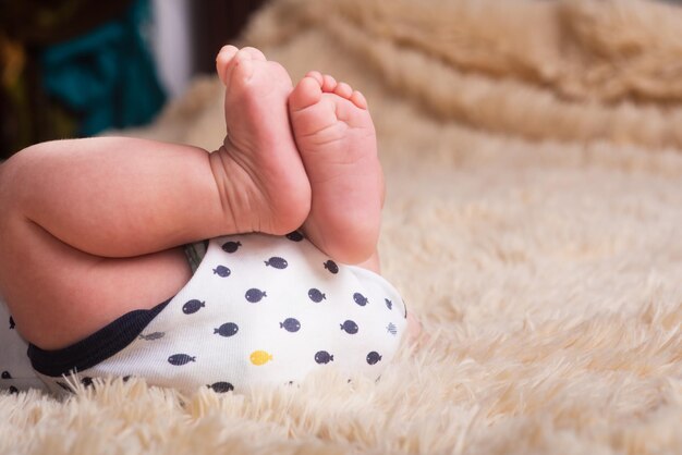 Jambes nues d'un nouveau-né sur un revêtement moelleux, léger, d'une tonne et chaud. Pieds de bébé nouveau-né mignon se bouchent. Place pour le texte, copyspace