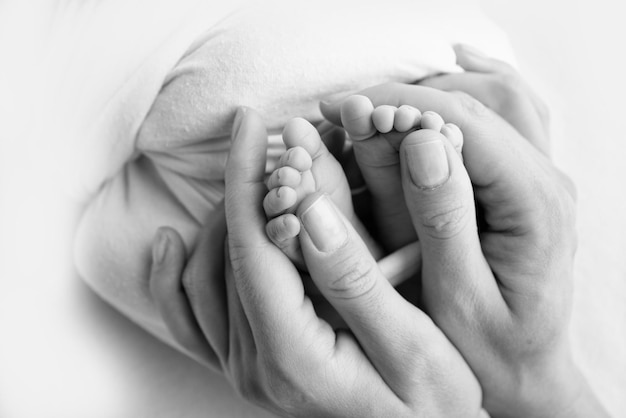 Jambes orteils pieds et talons d'un nouveau-né Avec les mains des parents père mère tient doucement les jambes de l'enfant Macro photographie gros plan Photo noir et blanc Photo de haute qualité