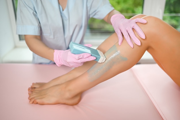 Photo jambes parfaites féminines avec une peau lisse ayant une procédure d'épilation à l'épilation à la cire dans un salon de beauté par une esthéticienne