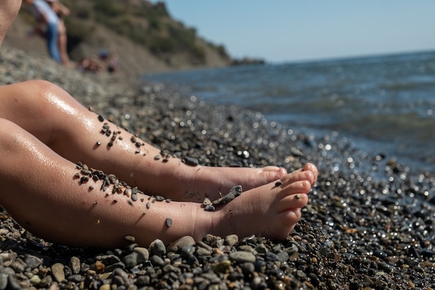 Jambes d'un petit enfant assis au bord de la mer.