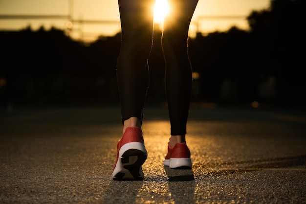 Les jambes et les pieds des femmes marchant en baskets sur l'asphalte au soleil couchant