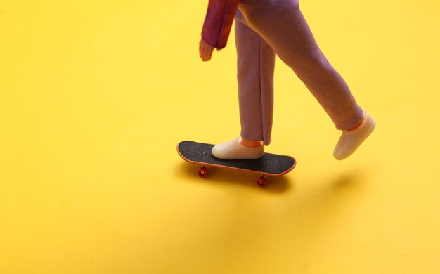 Jambes de poupée monter sur planche à roulettes sur fond jaune Minimalisme