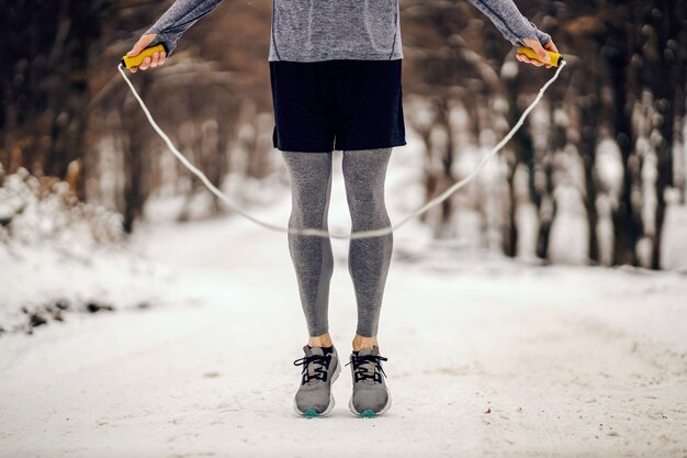 Jambes de sportif sautant la corde dans les bois le jour d'hiver enneigé. Fitness hivernal, temps enneigé