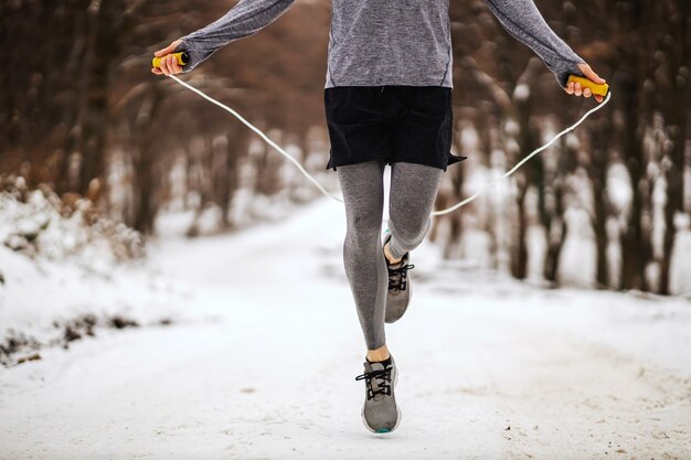 Jambes de sportif sautant la corde dans les bois le jour d'hiver enneigé.