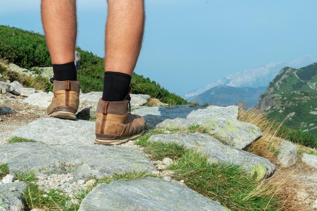 Jambes d'un touriste en bottes de trekking gros plan sur un rocher sur fond de montagnes, vue arrière