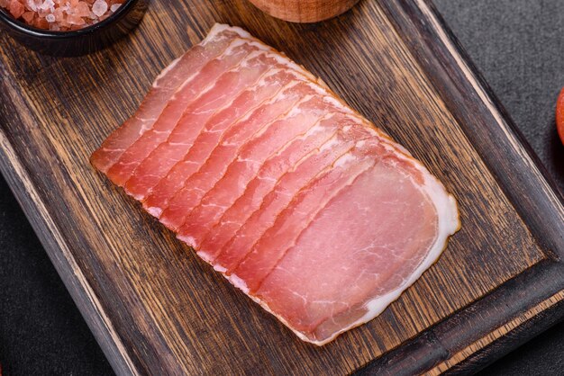 Jambon fumé sur une table en béton foncé avec ajout d'herbes aromatiques fraîches et d'épices produit naturel de la ferme biologique