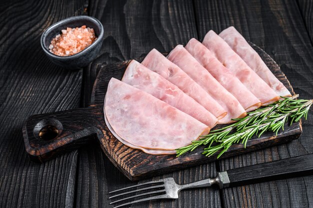 Jambon prosciutto tranché sur planche à découper en bois. Fond en bois noir. Vue de dessus.