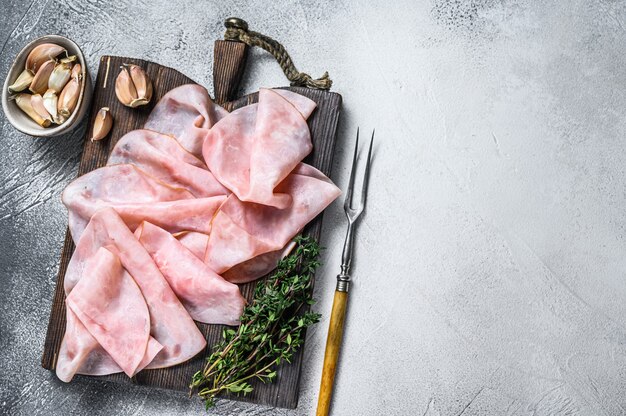 Jambon tranché mince sur une planche à découper en bois avec des herbes. Fond blanc. Vue de dessus. Espace de copie.