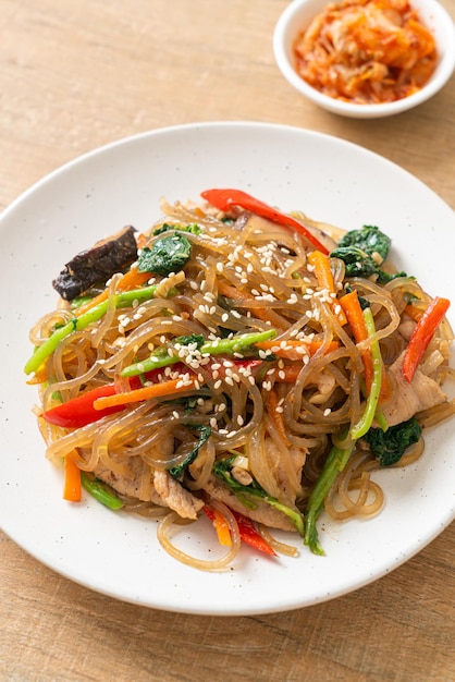 Photo japchae ou vermicelles coréens sautés aux légumes et au porc garnis de sésame blanc - style de cuisine traditionnelle coréenne