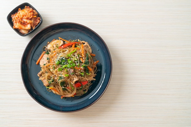 Photo japchae ou vermicelles coréens sautés aux légumes et au porc garnis de sésame blanc - style de cuisine traditionnelle coréenne