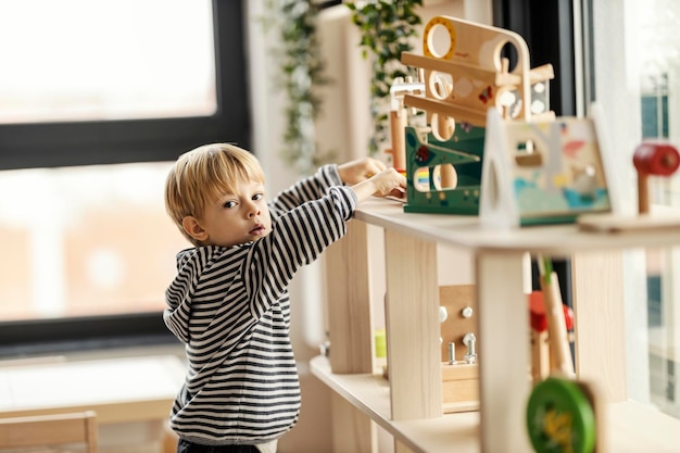 Un jardin d'enfants curieux prend un jouet montessori de l'étagère pour jouer avec
