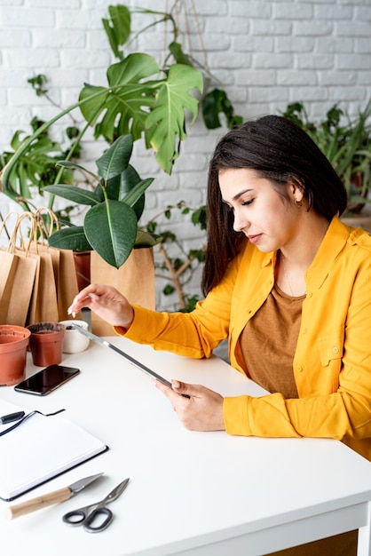 Jardinage domestique. Petite entreprise. Jardinier femme travaillant sur une tablette numérique entourée de plantes