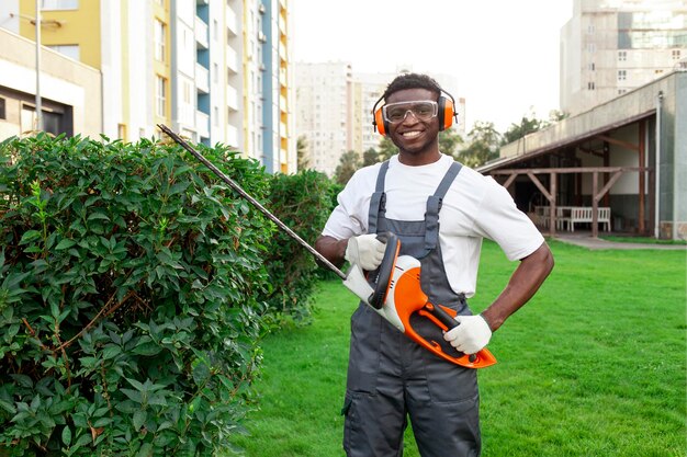 Photo un jardinier afro-américain en uniforme coupe des buissons avec un outil électrique.