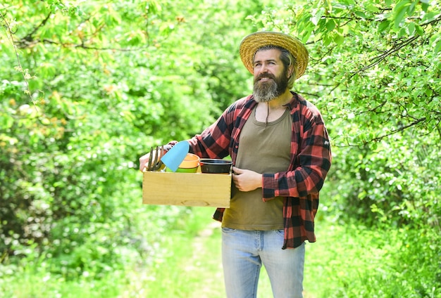 Jardinier agricole passe-temps et travail de jardinage. planter des semis dans le jardin. Les gens jardinent à la maison. Outils de jardin et fleurs sur le jardin verdoyant. homme dans les terres agricoles d'été avec boîte.