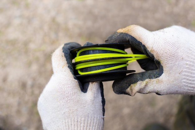 Le jardinier enroule la ligne de pêche autour de la tête de la tondeuse Remplacer les consommables des tondeuses à gazon