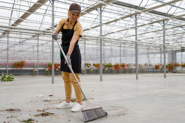 Jardinier féminin balayant le sol avec des balais en serre