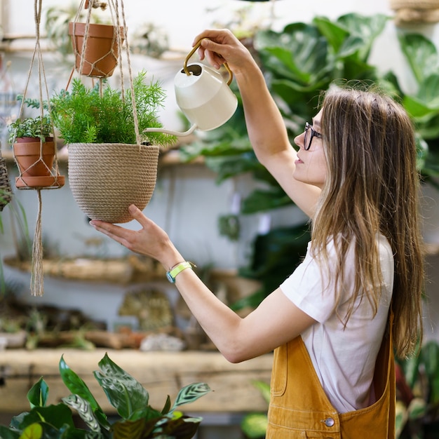 Jardinier fille arrosage plante en pot femme fleuriste étudiant prendre soin des plantes d'intérieur dans le jardin d'accueil