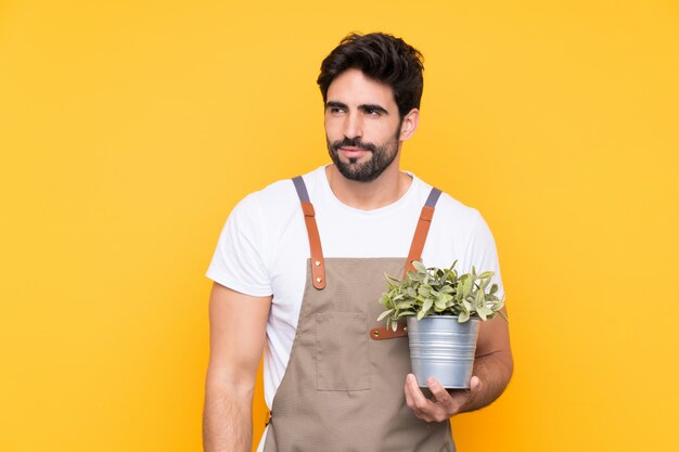 Jardinier homme avec barbe sur mur jaune isolé debout et regardant sur le côté