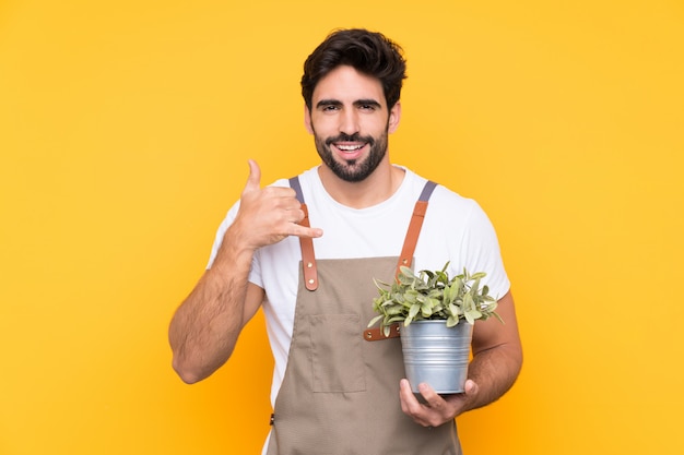 Jardinier homme avec barbe sur mur jaune isolé faisant geste de téléphone