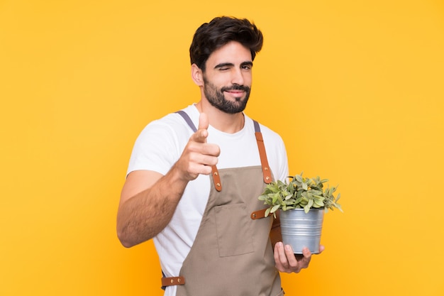 Jardinier homme avec barbe sur le mur jaune isolé pointe le doigt vers vous