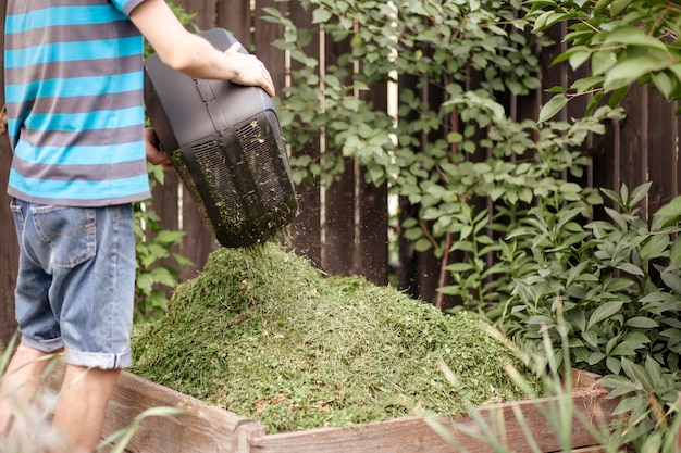 Jardinier jetant de l'herbe de la tondeuse à gazon dans le bac à compost Recyclage des déchets de jardin Couper l'herbe