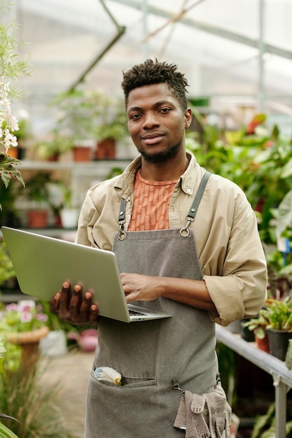 Jardinier avec ordinateur portable travaillant en serre