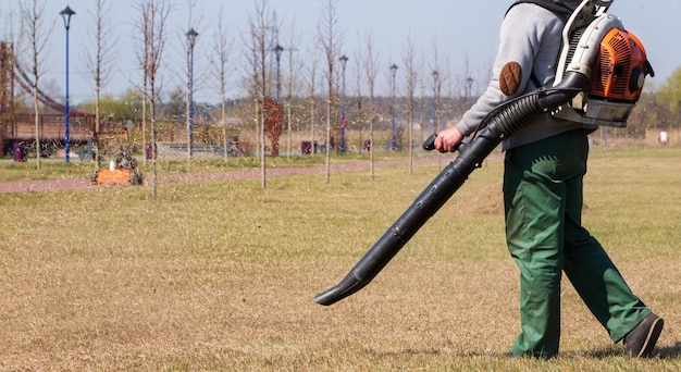 Jardinier avec souffleuse à air enlève l'herbe sèche de la pelouse dans le parc. Concept de soins de la pelouse.