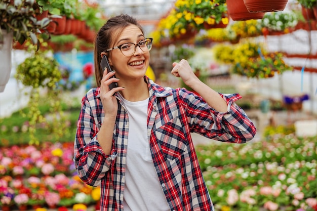 Jardinier souriant debout dans la serre et prenant les commandes d'un client sur téléphone intelligent.