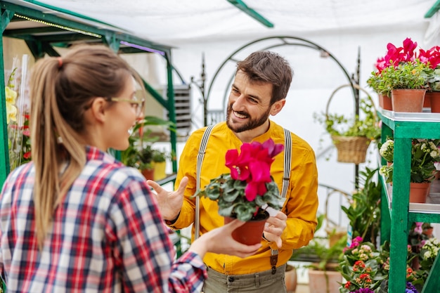 Jardinier souriant vendant des fleurs à un client en se tenant debout dans la serre