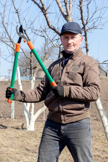 Le Jardinier Tient Dans Ses Mains De Grands Ciseaux Pour Couper Des Branches  D'arbres Un Homme Dans Le Jardin Avec Des Sécateurs