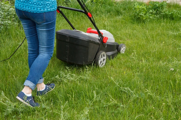 La jardinière travaille avec une tondeuse à gazon dans le jardin en été. Équipement de tondeuse à gazon. Outil de travail de soin de jardinier de tonte.