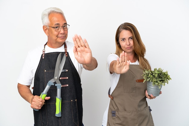 Jardiniers D'âge Moyen Tenant Une Plante Et Des Ciseaux Isolés Sur Fond Blanc Faisant Un Geste D'arrêt Niant Une Situation Qui Pense Mal