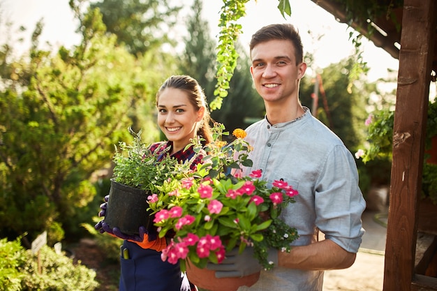 Les jardiniers heureux garçon et fille tiennent des pots avec des plantes dans de beaux jardins par une chaude journée ensoleillée.