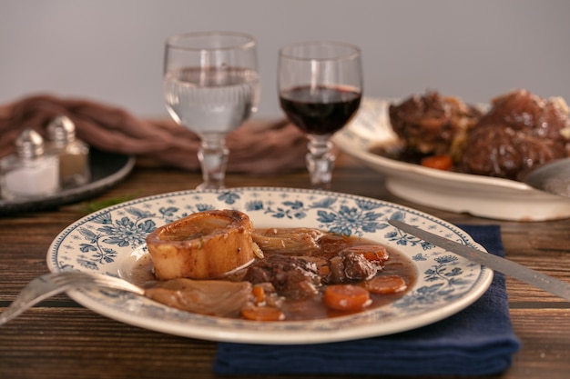 Jarret de bœuf bien cuit à la sauce au vin servi dans une assiette ancienne sur une table en bois