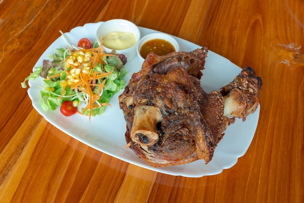 Jarret de porc frit croustillant ou cuisse de porc à l'allemande avec salade et sauce sur une table en bois de plat blanc