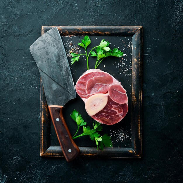 Jarret de veau cru frais coupé en croix pour faire de l'Osso Buco avec des épices et des herbes sur fond noir Vue de dessus Espace libre pour votre texte