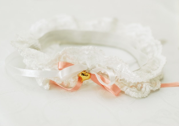 Photo jarretière en dentelle blanche pour la mariée avec un ruban de satin corail et un coeur doré sur fond blanc