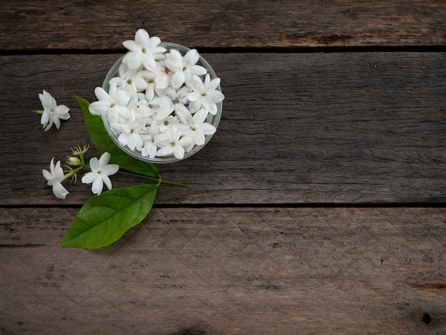 Jasmin flottant dans un verre clair sur fond en bois.