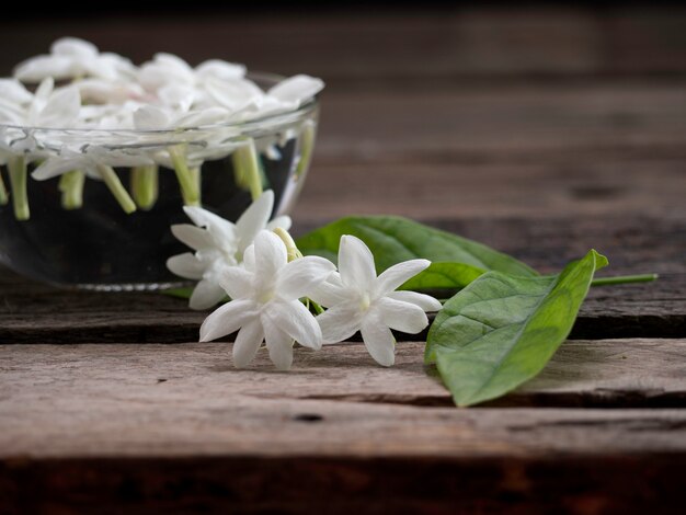 Jasmin flottant dans un verre clair sur fond en bois.