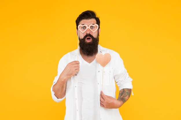 Je crois en l'amour joyeux anniversaire homme brutal avec barbe tomber amoureux rendez-vous romantique surpris hipster dans des lunettes de fête homme barbu hipster fond jaune coeur d'amour pour les vacances de la saint valentin