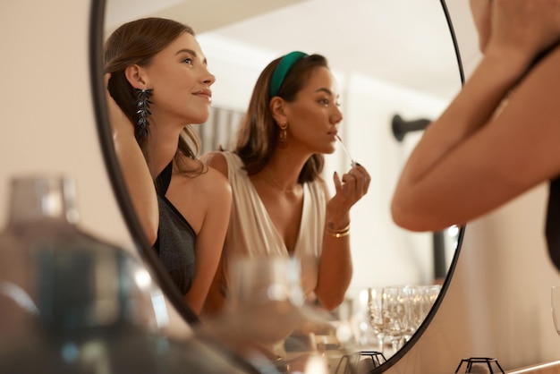 Je dois garder le meurtre intact Photo de deux jeunes amis debout ensemble et utilisant un miroir pour retoucher leur maquillage lors d'un dîner