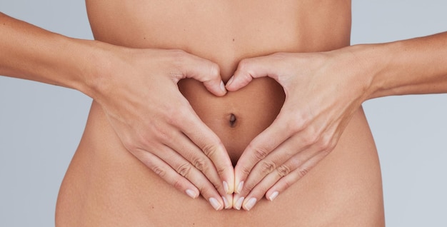 Je donne de l'amour à mon intestin, une photo coupée d'une femme inconnaissable debout seule dans le studio et faisant un geste en forme de cœur sur son ventre.