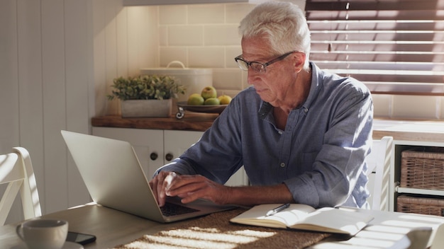 Je ferais mieux de le faire parvenir rapidement au client Photo d'un homme âgé assis seul dans la cuisine et utilisant son ordinateur portable pour travailler à domicile