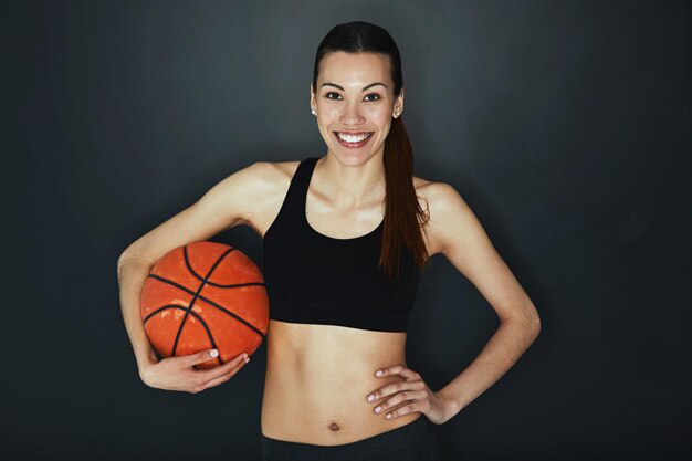 Je joue dur Prise de vue en studio d'une jeune femme tenant un ballon de basket sur un fond sombre