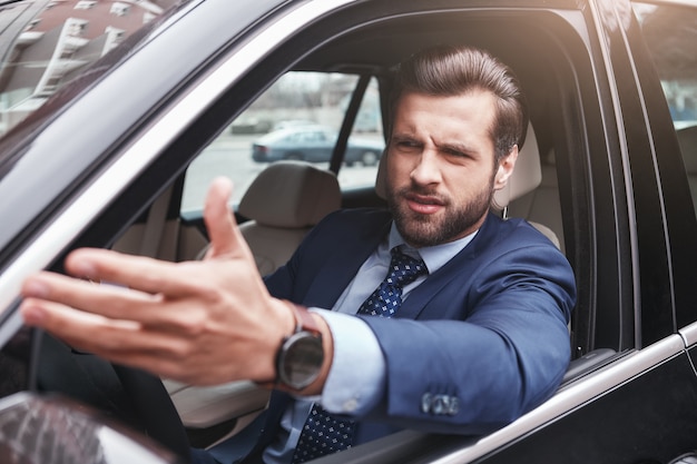 Je n'aime pas ça. Un homme d'affaires en colère et émotif en tenue de soirée fait des gestes et fait une grimace en conduisant sa voiture. Émotions négatives. Concept d'entreprise.