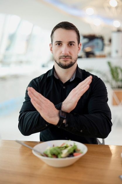 Je n'aime pas ce plat ! Homme sérieux attirant croisant ses mains dans le geste de désaccord. Il est fatigué de ne manger que des salades et des aliments sains. Mauvais concept de nourriture et de service. Restaurant sur le fond.