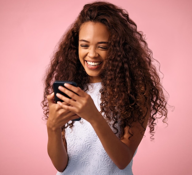 Je n'arrive pas à croire qu'il m'a envoyé un texto Prise de vue en studio d'une belle jeune femme utilisant son téléphone portable debout sur un fond rose